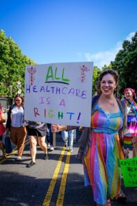 Person walking in a protest holding a sign that says "All healthcare is a right!"